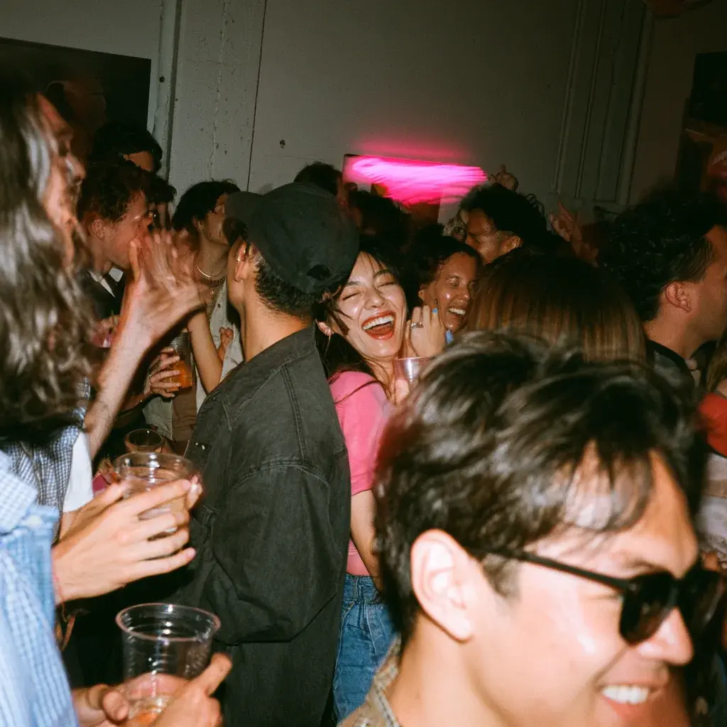Packed launch party crowd under a magenta neon sign